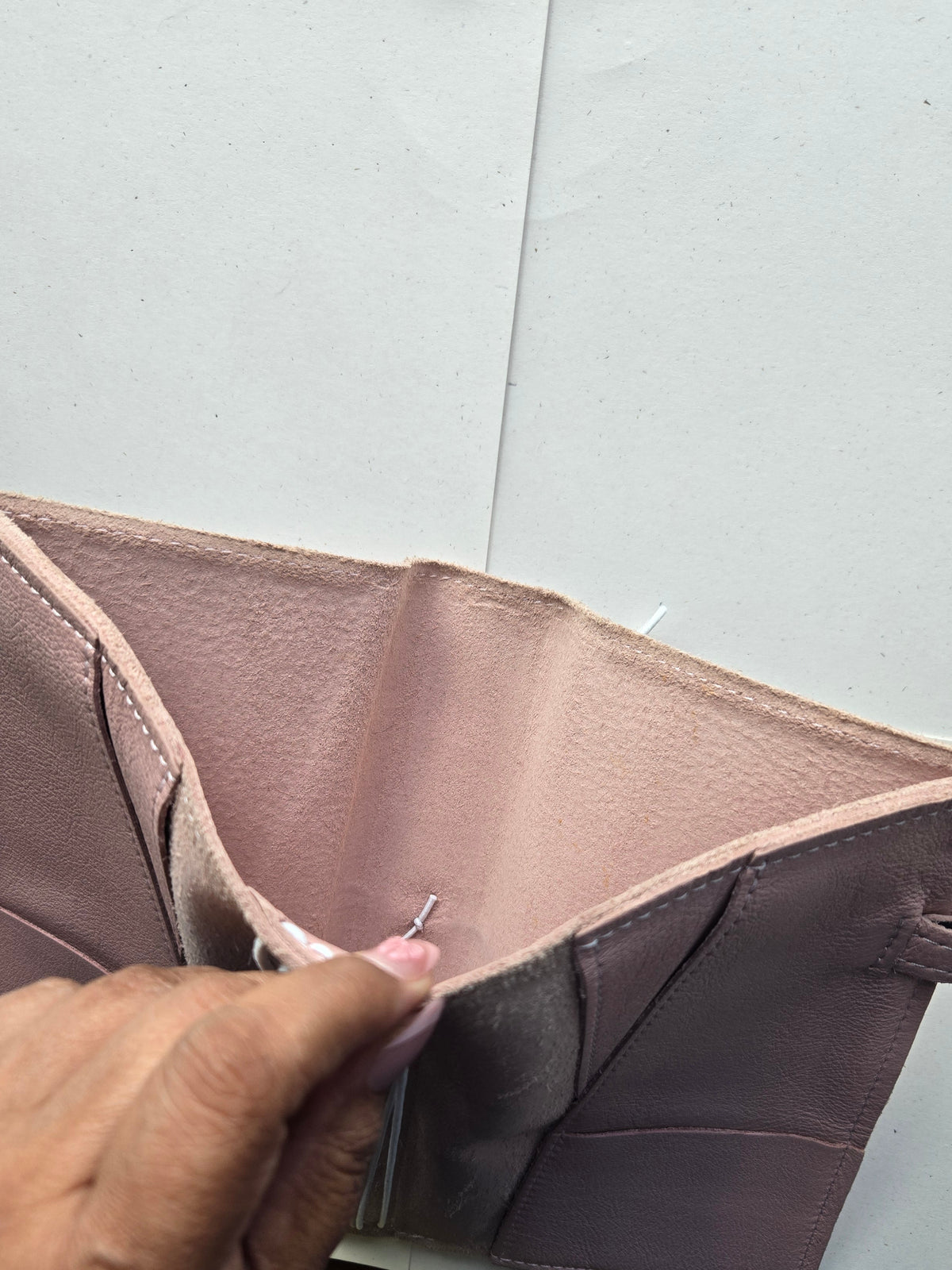 A close-up of a person's hand opening a brown textured leather wallet or card holder on a light gray surface.